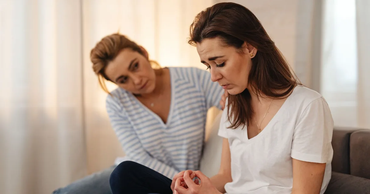 Mulher consolando outra angustiada sentada no sofá, sinais de que é hora de internar um dependente químico